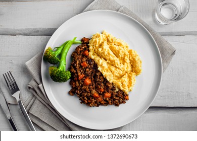 Plate Of Shepherd’s Pie On A White Wooden Table. Meal Made Of Smashed Potatoes, Minced Meat, Lentil And Vegetables. Top View, Above Shot.