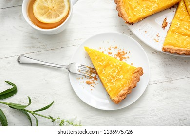 Plate with piece of tasty lemon pie and cup of tea on white wooden table