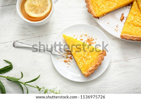 Plate with piece of tasty lemon pie and cup of tea on white wooden table