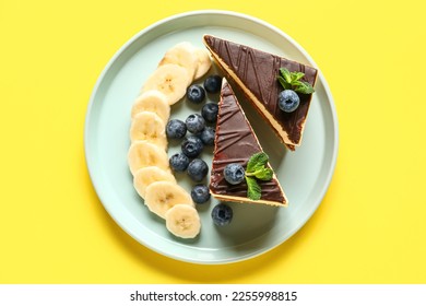 Plate with pieces of birds milk cake, blueberries, banana slices and mint leaves on yellow background - Powered by Shutterstock