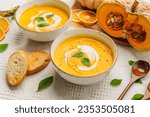 Plate of pumpkin carrot soup served with herbs, cream and crusty bread.