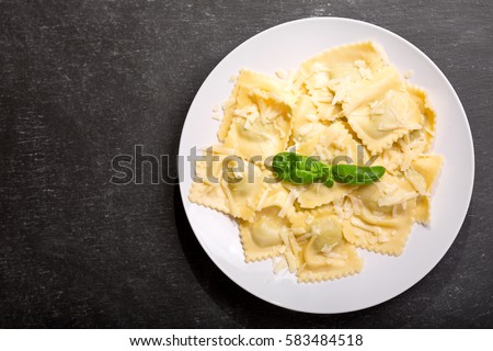 plate of ravioli with basil on dark background, top view