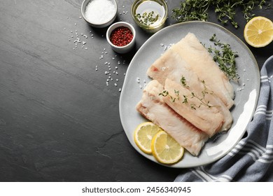 Plate with raw cod fish, microgreens, spices and lemon on dark textured table, flat lay. Space for text
