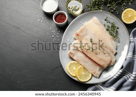 Plate with raw cod fish, microgreens, spices and lemon on dark textured table, flat lay. Space for text