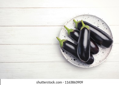 Plate with raw ripe eggplants on wooden background, top view