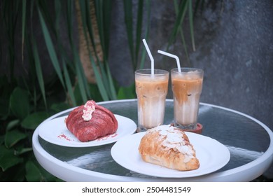 A plate of red velvet croissants with cream cheese topping and almond croissants, accompanied by an iced coffee latte - Powered by Shutterstock