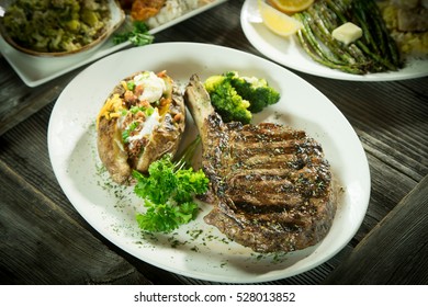 Plate With Ribeye Steak, Broccoli And Baked Potato On Wooden Table.