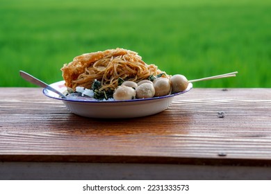 A plate of rice and side dishes on a table with rice fields in the background