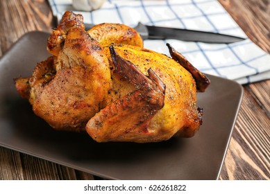 Plate with roasted beer can chicken on wooden background