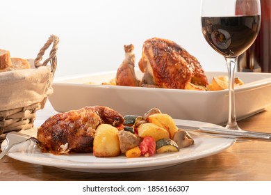 A Plate Of Rotisserie Chicken With Assorted Vegetables With Out Of Focus Glass Of Wine And Basket Of Bread