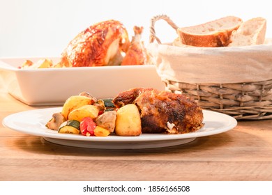 A Plate Of Rotisserie Chicken With Vegetables With Out Of Focus Basket Of Bread And Baking Dish