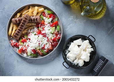 Plate with serbian shopska salad, grilled cevapi sausages and fries, top view on a grey concrete background, horizontal shot