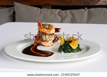 plate of sesame covered shrimp with mexican mole sauce fries and spinach on white tablecloth in a restaurant