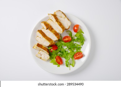 Plate Of Sliced Chicken Breasts With Rucola And Cherry Tomatoes On White Background