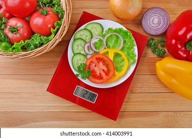 Plate with sliced fresh vegetables on digital kitchen scales over wooden background