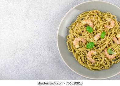 A plate with spaghetti and prawns on a stone table