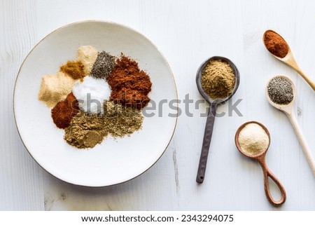 A plate and spoons with spices used to make a taco seasoning blend.