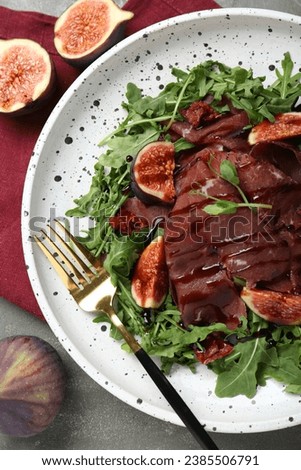 Plate of tasty bresaola salad with figs, sun-dried tomatoes, balsamic vinegar and fork on grey table, flat lay