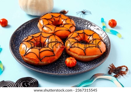 Plate of tasty donuts for Halloween with candies on blue background