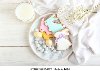 Plate with tasty Easter cookies in shape on bunny, gypsophila flowers and glass of milk on white wooden background