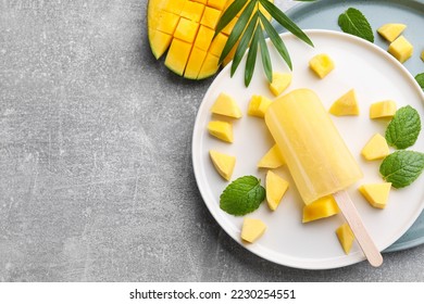 Plate of tasty fruit ice pop with mango on grey table, flat lay. Space for text