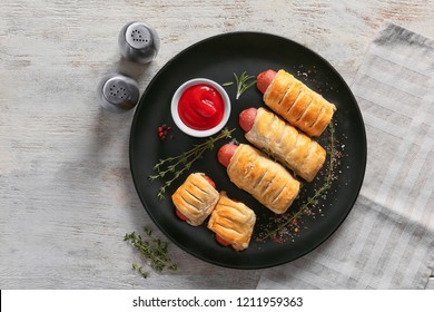 Plate with tasty sausage rolls and sauce on wooden table