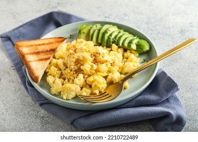 Plate With Tasty Scrambled Eggs, Avocado And Toast On Light Background