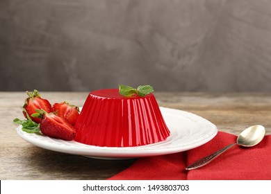 Plate of tasty strawberry jelly served on wooden table, space for text