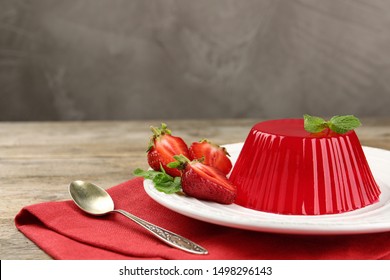 Plate of tasty strawberry jelly served on wooden table, space for text