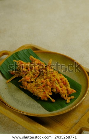 A plate of Tempoyak Ikan Teri or Otun on brown background. Anchovy fish with tempoyak, chili, onion and turmeric. Tempoyak made from fermented durian fruit. Makanan tradisional