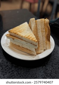 a plate of toasted sandwich triangles stacked on a white plate, with visible layers of peanut butter and coconut jam spread.