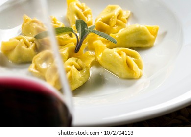 a plate of tortelli, a typical stuffed pasta from Piacenza, north Italy, with butter and fresh sage leafs. the plate is hidden by a glass of red wine  - Powered by Shutterstock