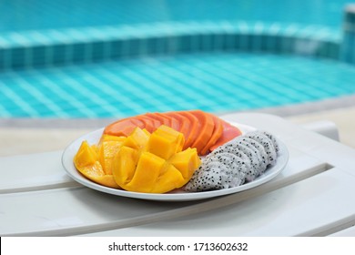 Plate With Tropical Fruits Near The Pool. Papaya, Mango, Dragon Fruit On A Plate On A Blue Pool Background. Thai Fruits.