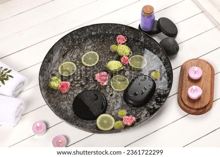 Plate with water, flowers, burning candles and lime slices on white wooden floor. Pedicure procedure