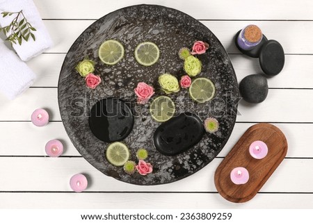 Plate with water, flowers, lime slices and burning candles on white wooden floor, flat lay. Pedicure procedure