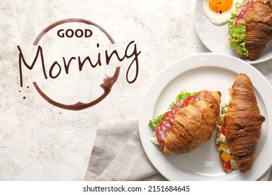 Plates with delicious croissant sandwiches and text GOOD MORNING on light background, top view