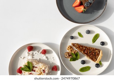 Plates with desserts close-up on a white background. Copy space. Pecan pie, meringue roll and chocolate cake are decorated with berries and mint leaves. Breakfast and tea - Powered by Shutterstock