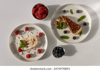 Plates with desserts close-up on a white background. Copy space. Pecan pie, meringue roll and chocolate cake are decorated with berries and mint leaves. Breakfast and tea - Powered by Shutterstock