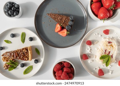 Plates with desserts close-up on a white background. Copy space. Pecan pie, meringue roll and chocolate cake are decorated with berries and mint leaves. Breakfast and tea - Powered by Shutterstock