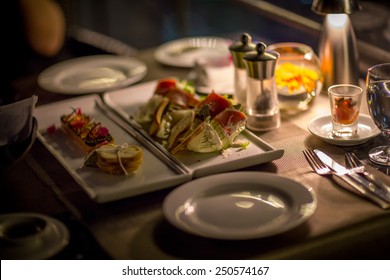 Plates and Dishes on the table in luxury restaurant. Sushi roll with salad. Romantic dinner with ambient light from candle.