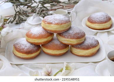 Plates with home baked berliner donuts with traditional yellow ring. Fluffy doughnuts made of rich sweet dough, stuffed with jam or vanilla cream; hellebores, olive branch and coffee in background. - Shutterstock ID 2195148951