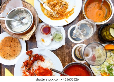 Plates Of Indian Food Leftovers On Wooden Table From Above.