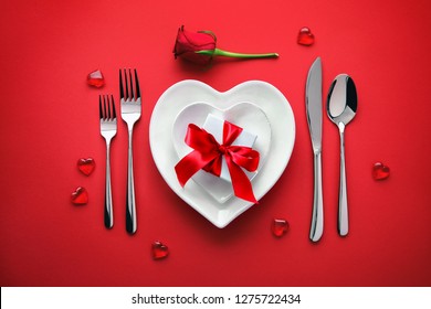 Plates in shape of heart, holidays table setting with a gift box on red background - Powered by Shutterstock