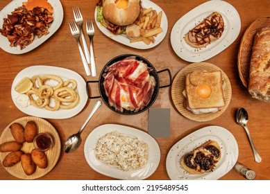 Plates And Trays Of Typical Recipes Of Spanish Gastronomy With Croquette Tapas, Grilled Ear, Alioli Potatoes, Andalusian Squid, Toast, Sandwich With Fried Egg, Hamburgers And Scrambled Eggs With Ham