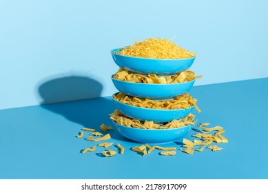 Plates with uncooked pasta stacked one above each other  on a blue table. Variety of pasta in blue plates in bright light on a colorful background. - Powered by Shutterstock