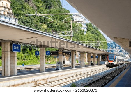Platform view of Como train station in northern Italy featuring a clear “Como” station sign, tracks, and shelter. Great for travel, transport, and tourism visuals of Italian destinations