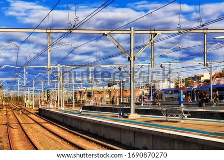 Platforms of train station in Greater Sydney with daily commuters and city visitors boarding train on open platform under blue sky - modern urban transportation system.