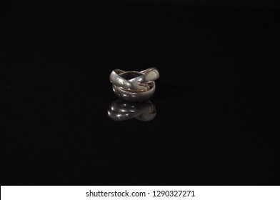 Platinum trinity wedding ring on a black refelctive surface. 