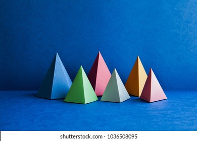 Platonic solid geometric figures. Three-dimensional pyramid rectangular objects on blue background. Yellow blue pink violet red colored tetrahedron abstract shapes objects.