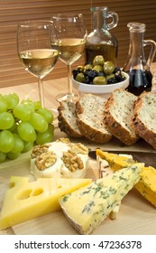 A Platter Of Mediterranean Food Including Cheese, Grapes, White Wine, Bread, Olives, Olive Oil And Balsamic Vinegar. Shot In Beautiful Warm Light With The Focus On The Cheese In The Foreground.